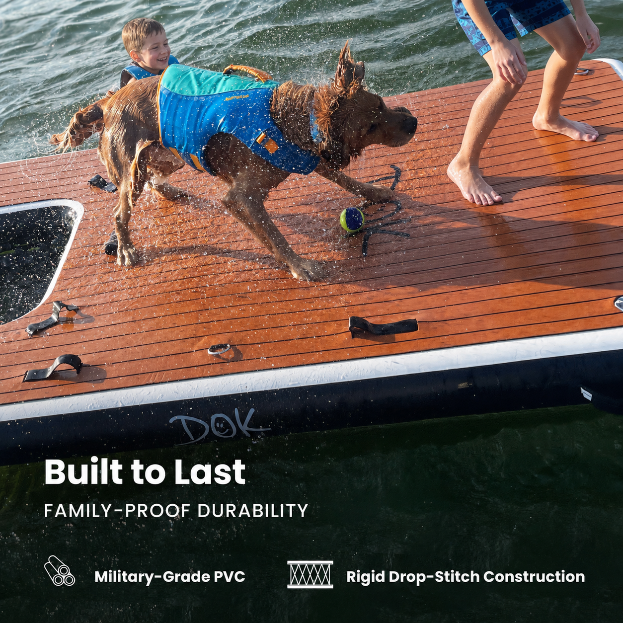 A dog wearing a blue life vest runs across a wooden deck on a floating platform in the water, with a child and another person partially visible. Text at the bottom reads 'Built to Last Family-Proof Durability' with feature callouts for military-grade PVC and rigid drop-stitch construction.
